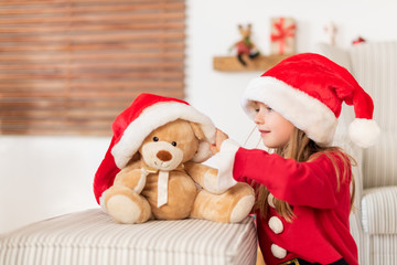 Cute young girl wearing santa hat playing with her christmas present, soft toy teddy bear. Playful kid at christmas time with soft toy.