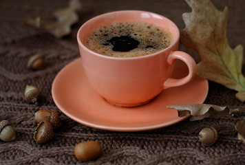 A ceramic cup of coffee, dry autumn oak leaves and acorns are on a warm knitted jersey with a beautiful pattern. Handmade.