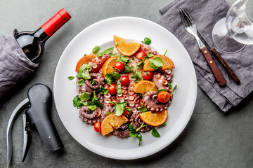 Whole octopus salad with orange, tomatoes and cress salad on white plate. Top view