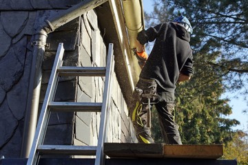 Ein Dachdecker zersägt und demontiert die alte Dachrinne