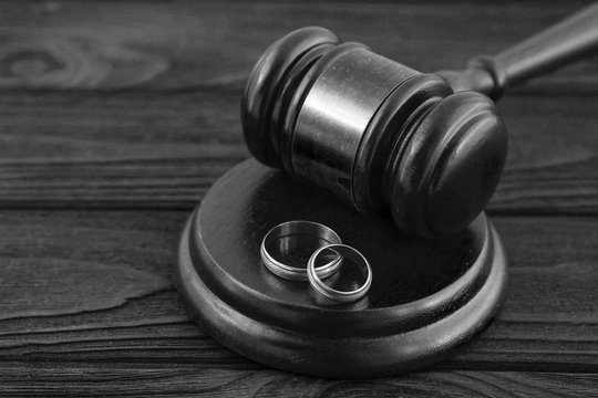 judge's hammer, a pair of wedding rings on a wooden table background. divorce, family conflicts, family law.
