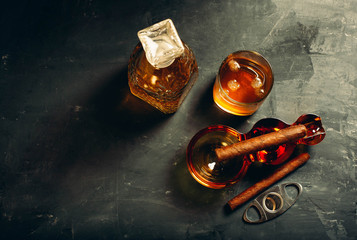Strong alcoholic drink, scotch whisky in old fashion glass and decanter with smoking cigar in ashtray on gray concrete background