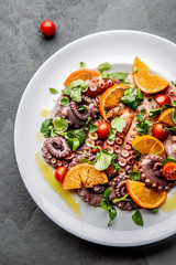 Whole octopus salad with orange, tomatoes and cress salad on white plate. Top view