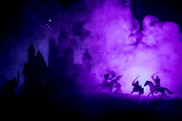 Naklejka na ściany i meble Medieval battle scene with cavalry and infantry. Silhouettes of figures as separate objects, fight between warriors on dark toned foggy background with medieval castle. Night scene. Selective focus