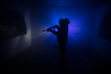 Silhouette of man with assault rifle ready to attack on dark toned foggy background or dangerous...