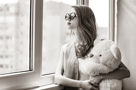 Sad grunge girl near window with toy bear. Image in black and white color style
