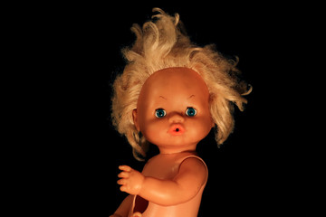 Portrait of an old doll on a black background. Plastic doll face in darkness.