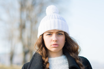 Beautiful teenage girl in coat and white knitted beanie hat, closeup portrait, no retouch, natural lighting