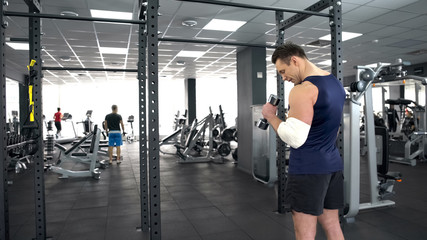 Strong man with injured elbow training with dumbbell in gym, recovery, strength