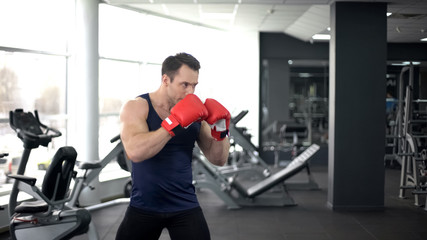 Fototapeta premium Muscular boxer in gloves training in gym, doing fighting stance, sport spirit