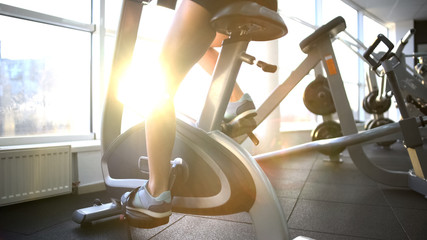 Female legs training on stationary bike, burning calories, cardio exercise