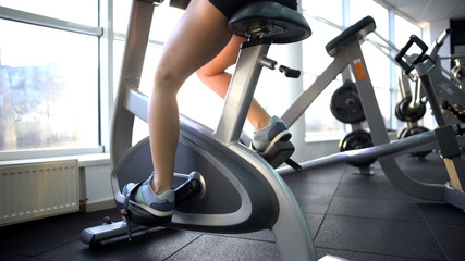 Womans legs training on stationary bike, burning calories, cardio exercise