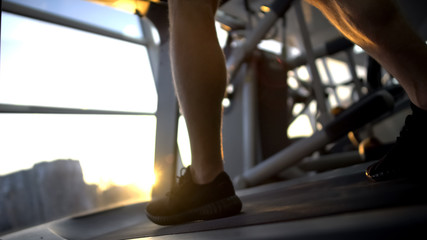 Fototapeta na wymiar Sportsman legs walking on treadmill, sunset training after work, stress relief
