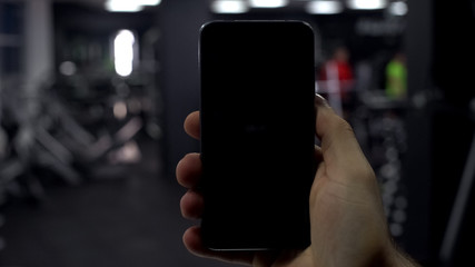 Male hand with cellphone in gym, fitness application results, black screen