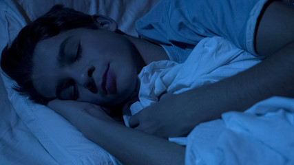 Closeup of male teenager face sleeping deeply at night time, feeling relaxed