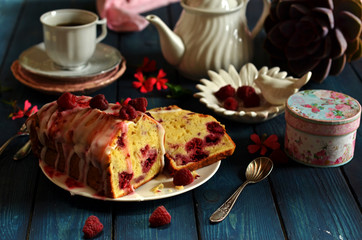 Fruit cake with raspberries on a blue wooden background. A cup of coffee on a white plate