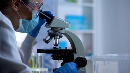 Lab technician examining test sample through microscope new medicine development