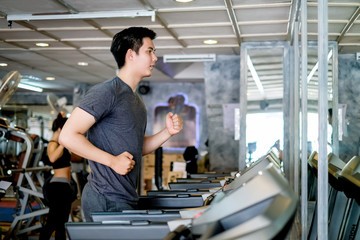 Asian man running in machine treadmill at  gym. Side view