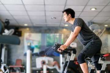 Fototapeta na wymiar Asian man exercising on stationary bike at gym.
