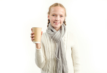 Teen girl holding a paper cup for hot drinks on a light background. Girl 13 years old dressed in a warm winter sweater and scarf.