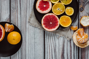 Delicious various types of citrus fruit in plates on wooden background