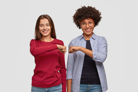 Multiethnic young women give fist bump to each other, show they are friendly team, have positive expressions, demonstrate agreement, dressed in casual clothing. Handshake and friendship concept