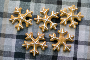 Painted traditional Christmas gingerbreads arranged on checkered tablecloth, group of snowflakes, white sugar icing