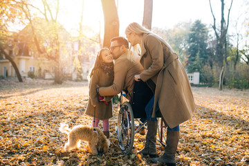 Disabled father in wheelchair enjoying with his daughter, wife and dog outdoors in park.