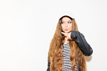Teenage girl with long hair making a kissy face and pointing to her side. Studio lighting, mild retouch.