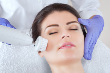 Obraz na płótnie Canvas The cosmetologist makes the Hardware face cleaning procedure with a soft rotating brush of a beautiful, young woman in a beauty salon. Cosmetology and professional skin care.