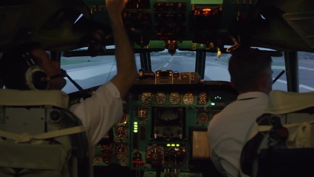 Medium shot of male pilots in uniform taking off headsets and turning off switches on instrument panel of airplane, then leaving cockpit