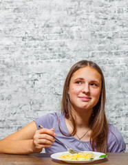 portrait of young teenager brunette girl with long hair Eating Spaghetti pasta with cheese on gray wall background