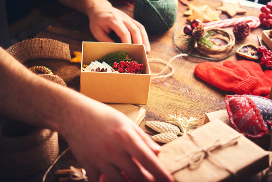 Christmas Background. A Lot Of Christmas Stuff With Gift Boxes. Man's Hands Holding Open Gift Box A Preparing Christmas Gifts. Christmas Preparation Concept