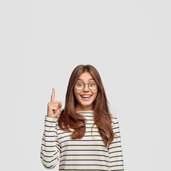 Isolated shot of cheerful Caucasian woman with straight hair, shows free space, points with index...