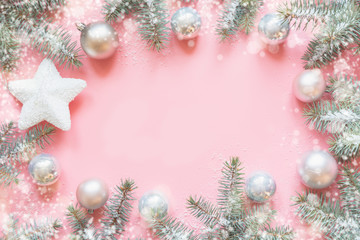Fototapeta premium Christmas frame made of fir branches, festive white decorations,white star balls on pink table. Xmas background. Flat lay. Top view with copy space