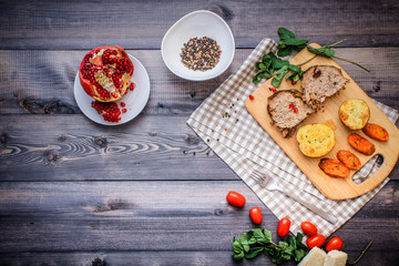 On a cutting board, slices of baked meat, baked potatoes and carrots, linen checkered napkin and cherry tomatoes on a dark graphite surface