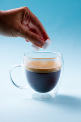 Hand holding two cubes of sugar over cup of coffee