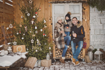 Russian young family enjoying their holiday time together, decorating Christmas tree outdoors in warm clothes, arranging the christmas lights and having fun. mother father and son meet new year