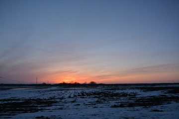 Obraz premium The end of a cold winters day with the sun behind the horizon and snow covered farm fields resting for the off season. 