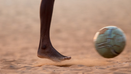 Kids playing football barefoot on sand