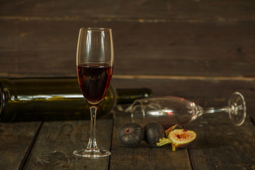 Wine in a glass an empty bottle of figs on a dark wooden background. A glass of wine on a wooden table.