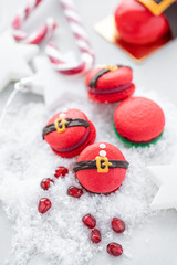 Fototapeta na wymiar Funny cookie in the form red santa belly on gray table sprinkled with snow. Modern european French cuisine. Christmas theme, Merry Christmas card. New year mood. Variety of sweet macaroons.