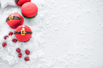 Obraz na płótnie Canvas Funny cookie in the form red santa belly on gray table sprinkled with snow. Modern european French cuisine. Christmas theme, Merry Christmas card. New year mood. Variety of sweet macaroons. copy space