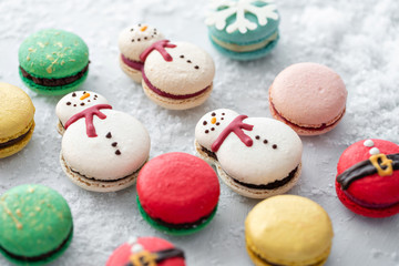 Variety of sweet macaroons on gray table sprinkled with snow. Modern european French cuisine. Christmas theme, Merry Christmas card. New year mood. lights of garland bulbs