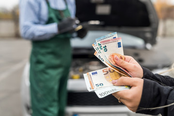 Euro banknotes in female hands on car engine background