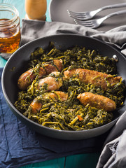 Italian sausages with rapini broccoli in a skillet with table setting on green wooden table