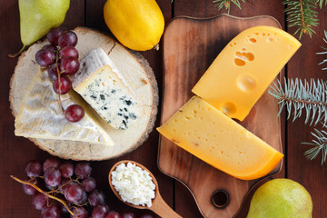 Various types of cheese and fruits on wooden boards and Christmas tree twigs. Swiss cheese, dorblu, camembert and cottage cheese for Christmas. Dairy products, lemon, grapes and pears. Top view