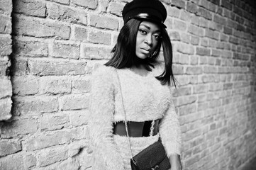 African american woman at violet dress and cap posed outdoor against brick tonel.