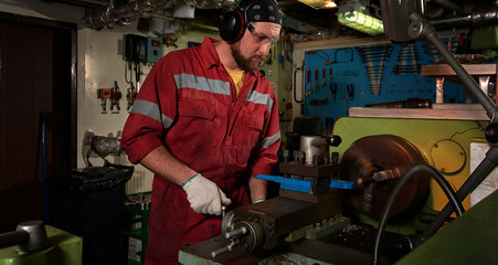 Worker in red uniform operating in manual lathe in metal big workshop.