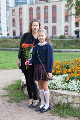 Full-length portrait of Caucasian mother and daughter going back to school together, schoolchild in uniform holding flower